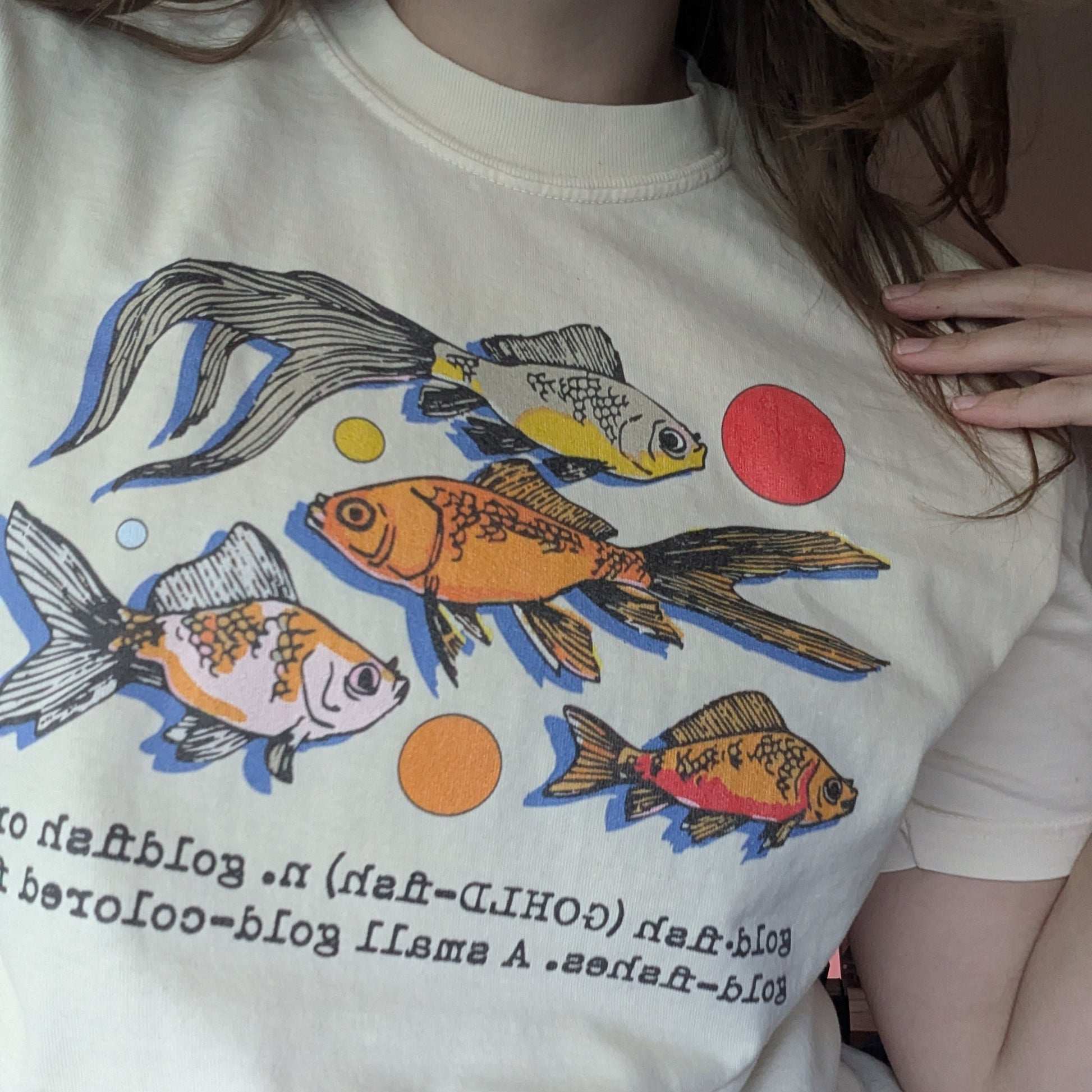 Person wearing a white t-shirt with colorful fish graphics and text.