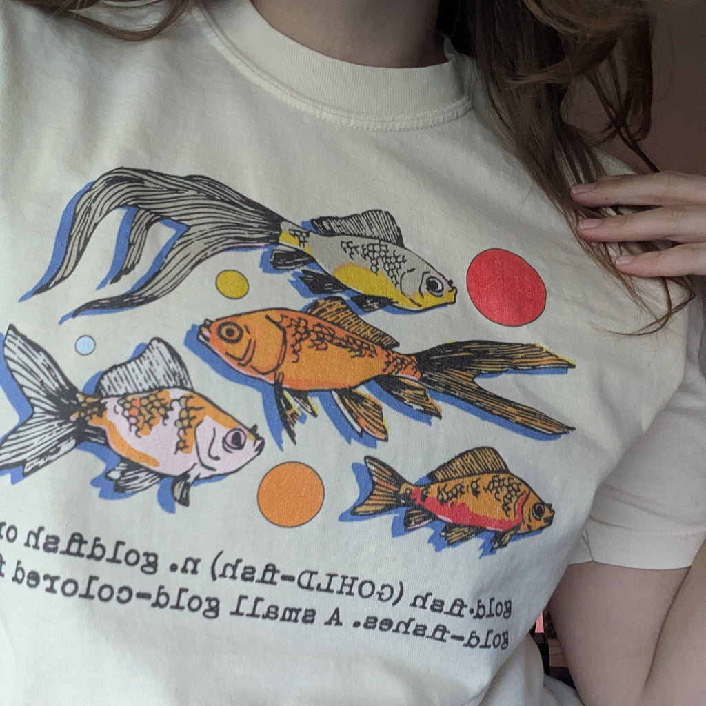 Person wearing a white t-shirt with colorful fish graphics and text.